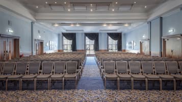 A large conference room with rows of chairs, a patterned carpet, and a view through a large window.