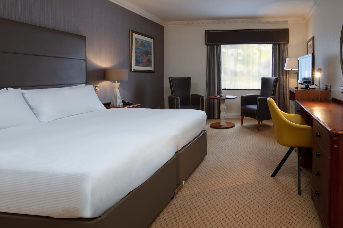 A hotel room with a large bed, a desk with a chair, a small table, and a TV.