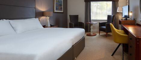 A hotel room with a large bed, a desk with a chair, a small table, and a TV.