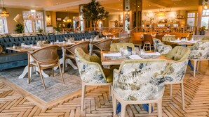 A spacious restaurant with high ceilings, a central seating area with cushioned sofas, and a variety of dining tables and chairs. - Belton Woods Hotel, Spa & Golf Resort (Grantham)