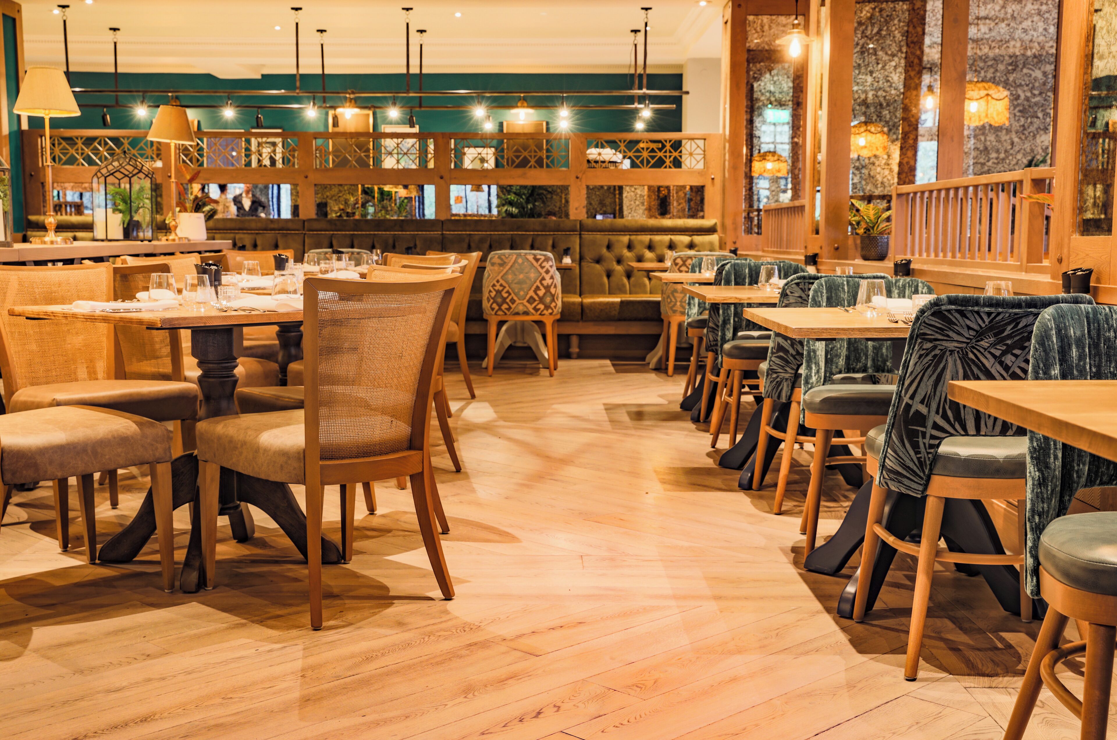 Un restaurante con mesas y sillas de madera, una pared verde y luces colgantes.