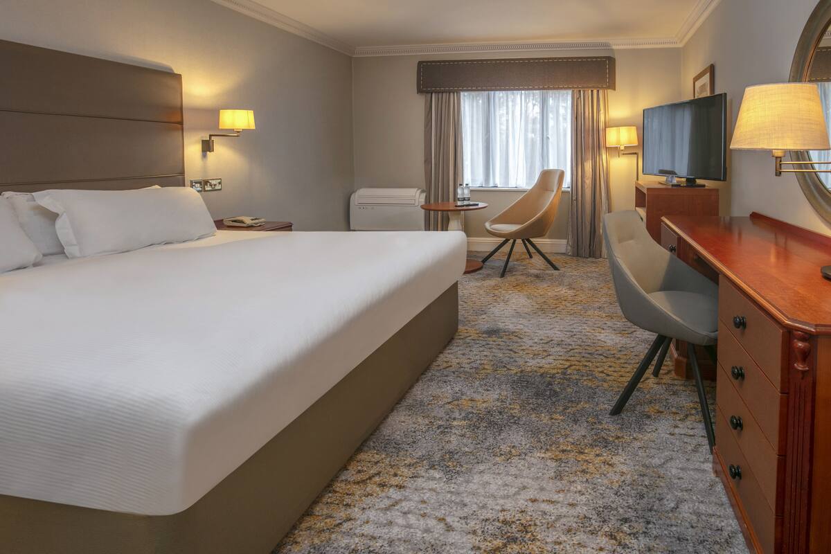 A hotel room with a large bed, a desk, a chair, a television, and a window with curtains.