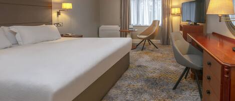 A hotel room with a large bed, a desk, a chair, a television, and a window with curtains.