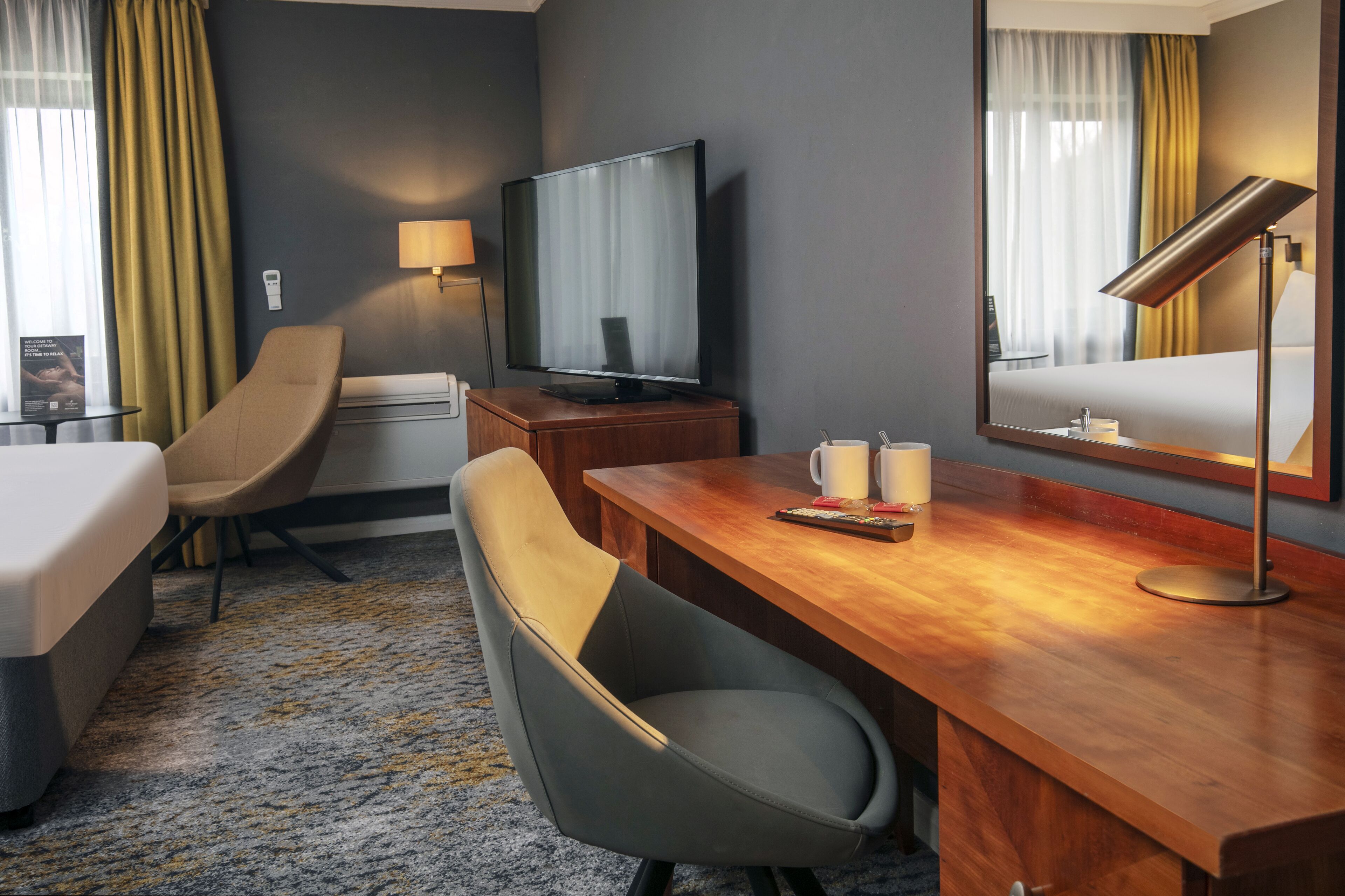 Une chambre d’hôtel équipée d’un lit, d’un bureau, d’une chaise, d’une télévision, d’une lampe et d’un miroir.