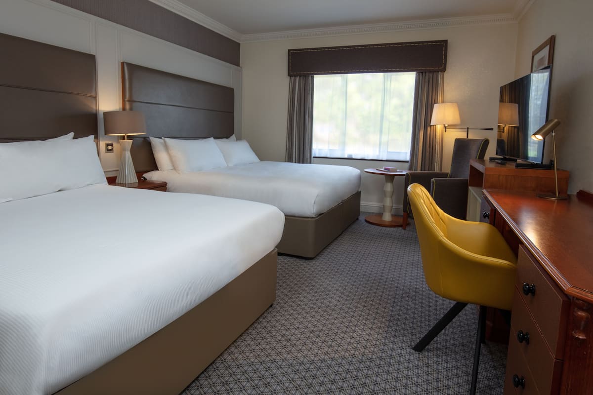 A hotel room with two beds, a desk, a chair, and a TV.