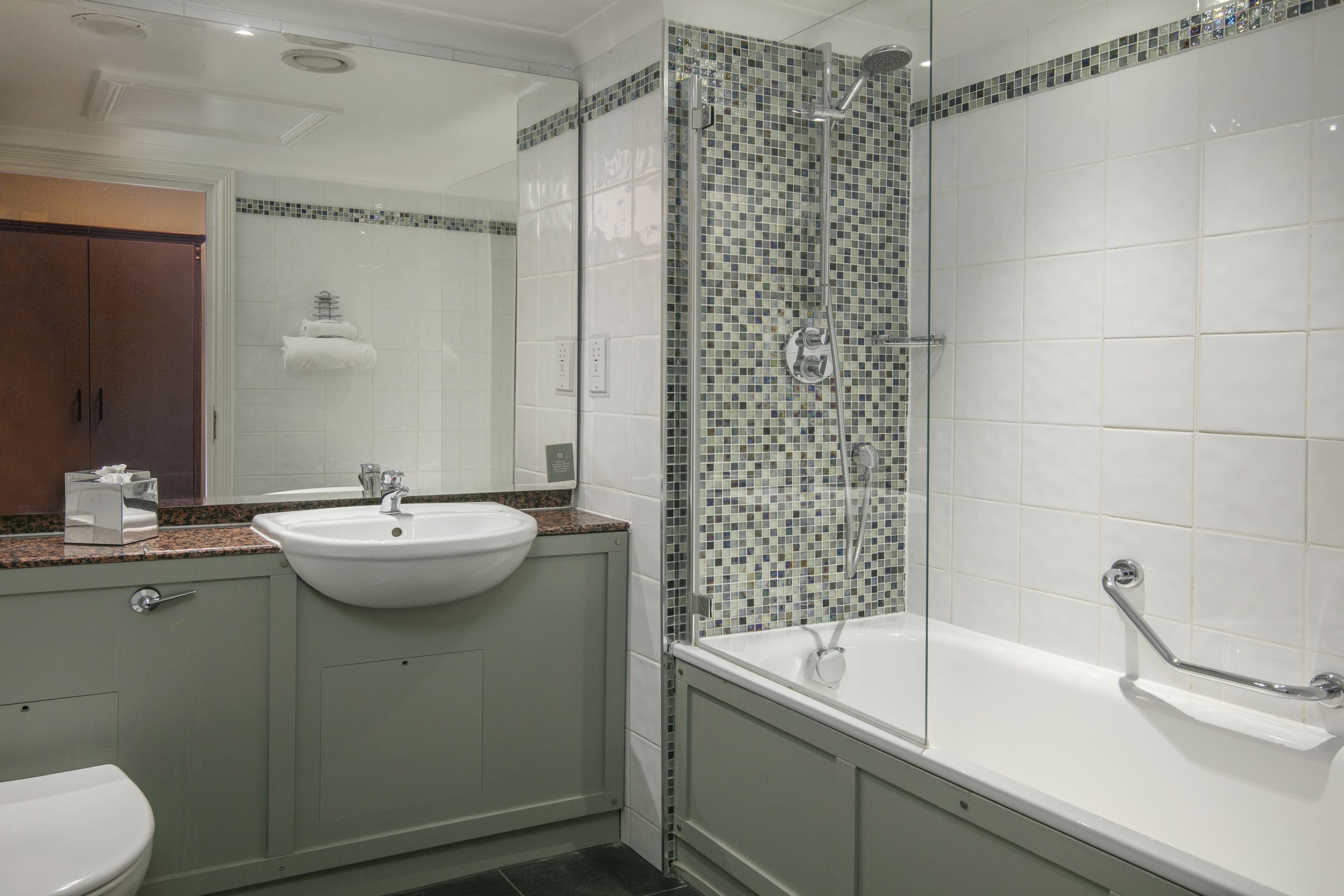Un baño moderno con lavamanos blanco, ducha con cerramiento de vidrio y bañera con barandilla.