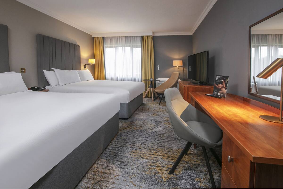 A hotel room with two beds, a desk with a chair, a TV, and a large mirror.