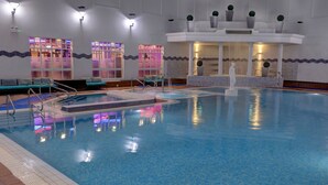 An indoor swimming pool with clear water, a lifeguard stand, and a seating area with blue cushions. - Belton Woods Hotel, Spa & Golf Resort (Grantham)