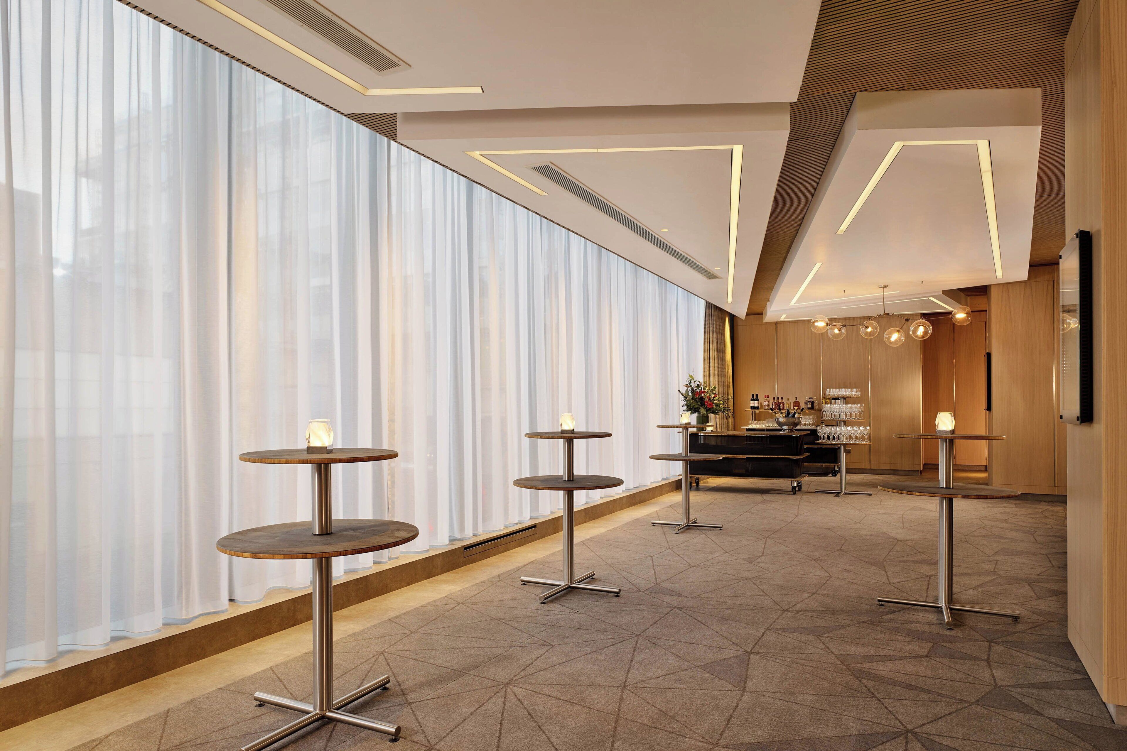Eine moderne Hotelhalle mit großen Fenstern, einer Bar und mehreren runden Tischen.