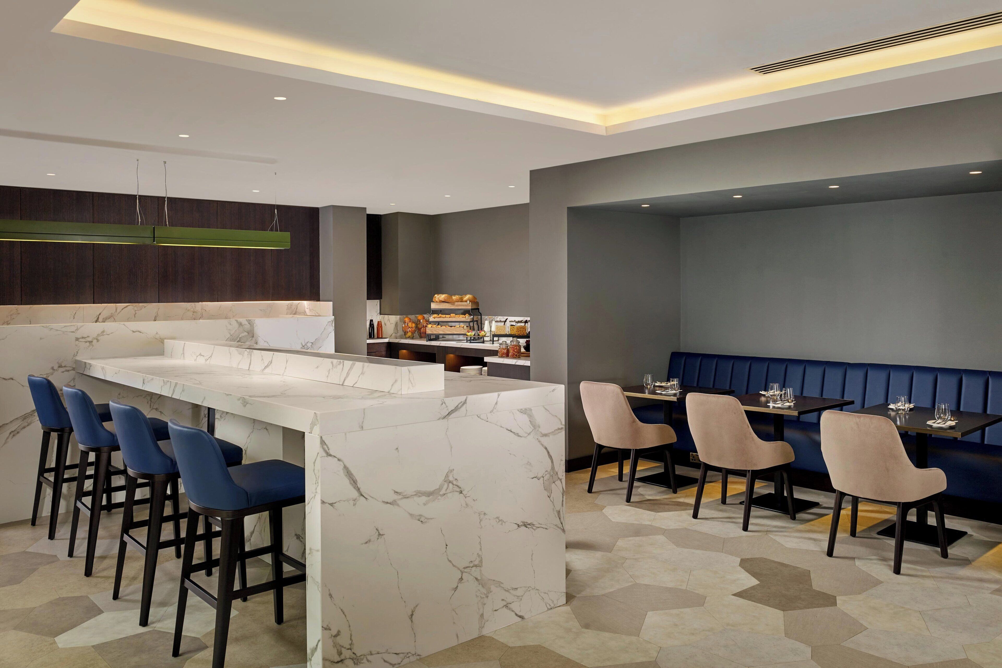 A modern bar area with marble countertops, bar stools, and a seating area with tables and chairs.