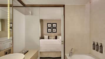 Une chambre d’hôtel avec un grand lit, une salle de bain séparée avec une baignoire, un meuble-lavabo avec un miroir et un placard à pharmacie fixé au mur.