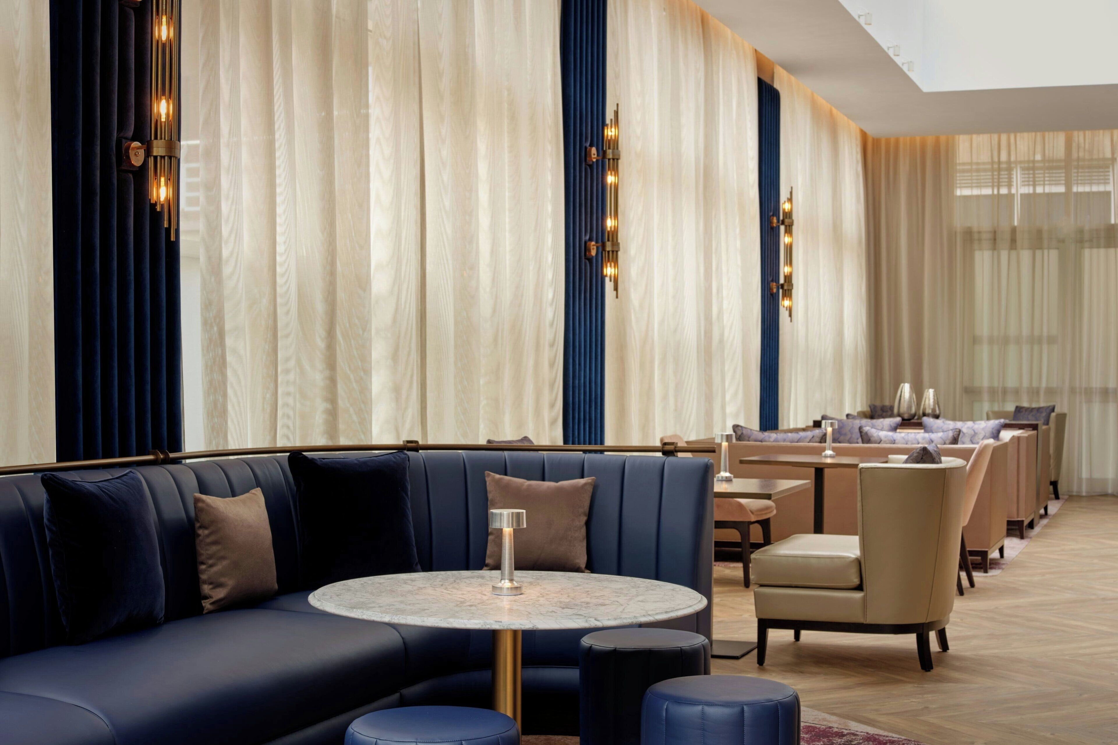 A modern hotel lobby with a curved sofa, round tables, and a dining area.