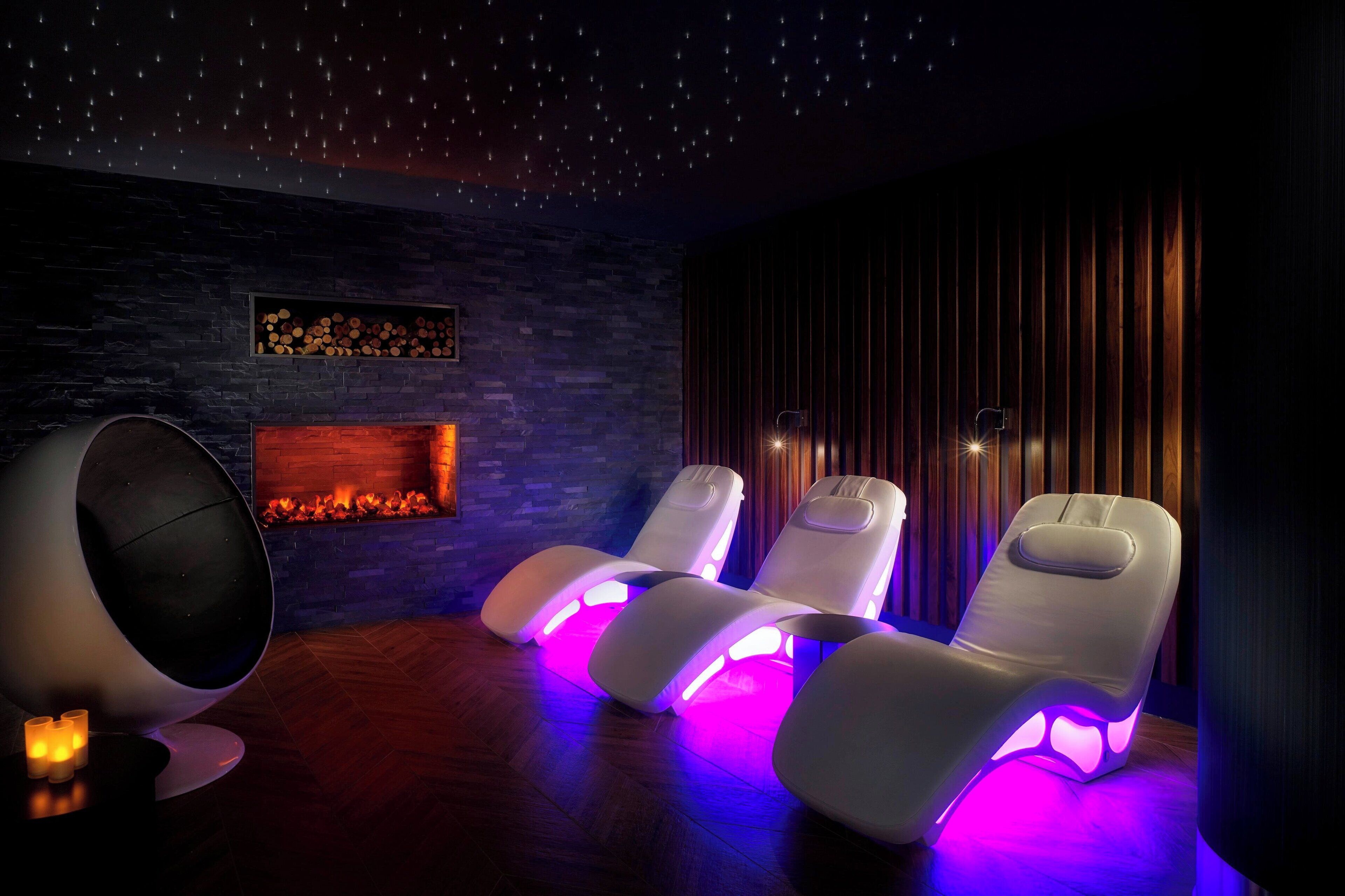 Una habitación con chimenea, tres sillones reclinables con iluminación integrada y un techo que simula un cielo estrellado.