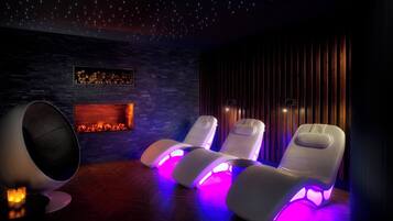 Una habitación con chimenea, tres sillones reclinables con iluminación integrada y un techo que simula un cielo estrellado.