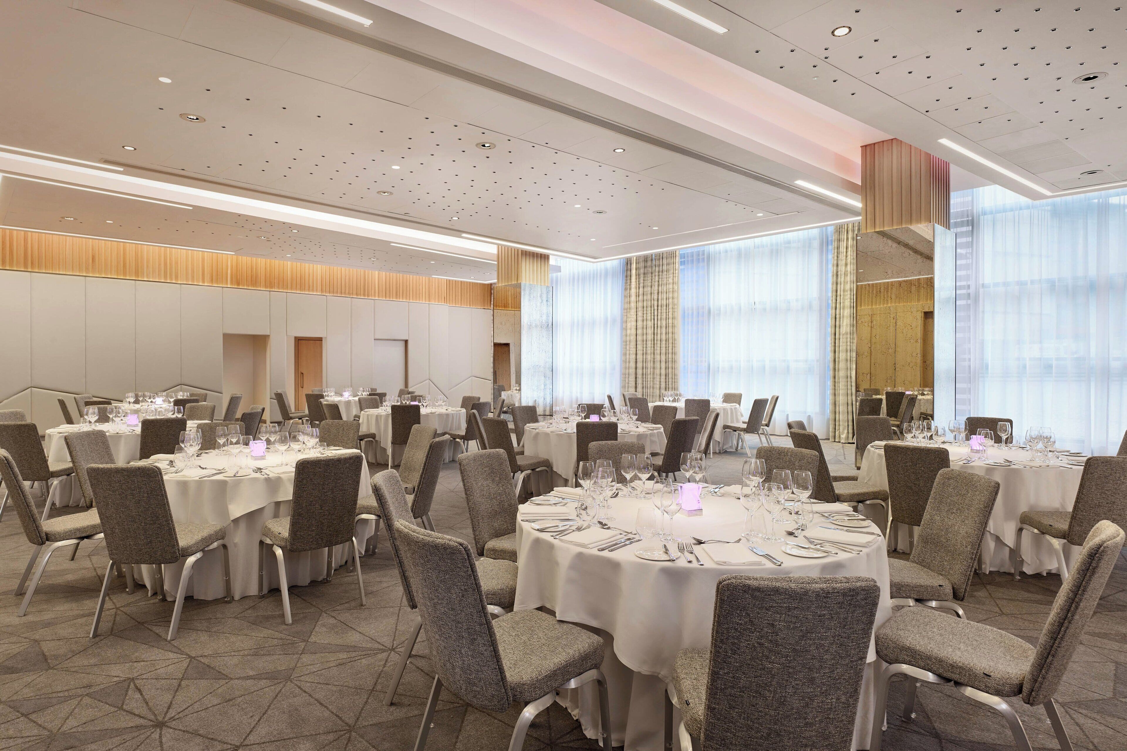 A banquet hall with round tables, chairs, and a high ceiling with recessed lighting.