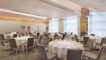A banquet hall with round tables, chairs, and a high ceiling with recessed lighting.