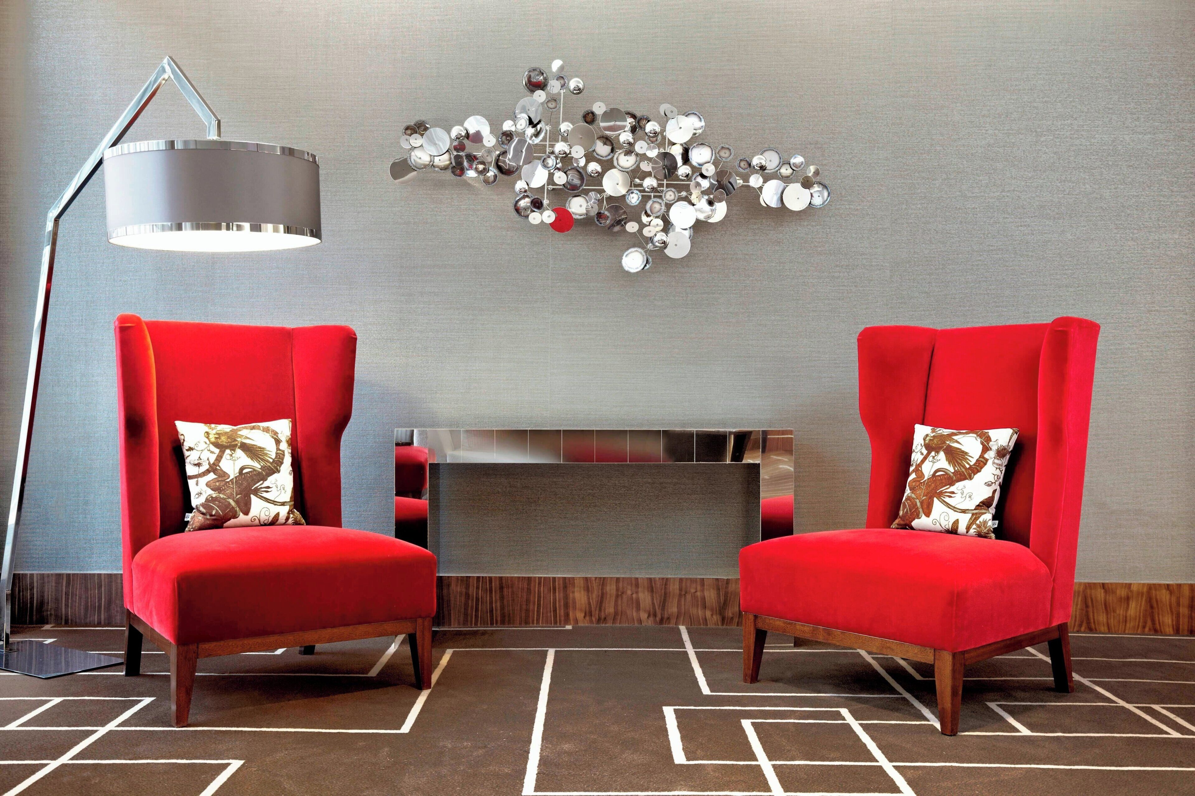 Una habitación moderna con dos sillas rojas, una lámpara de pie y un elemento decorativo en la pared.