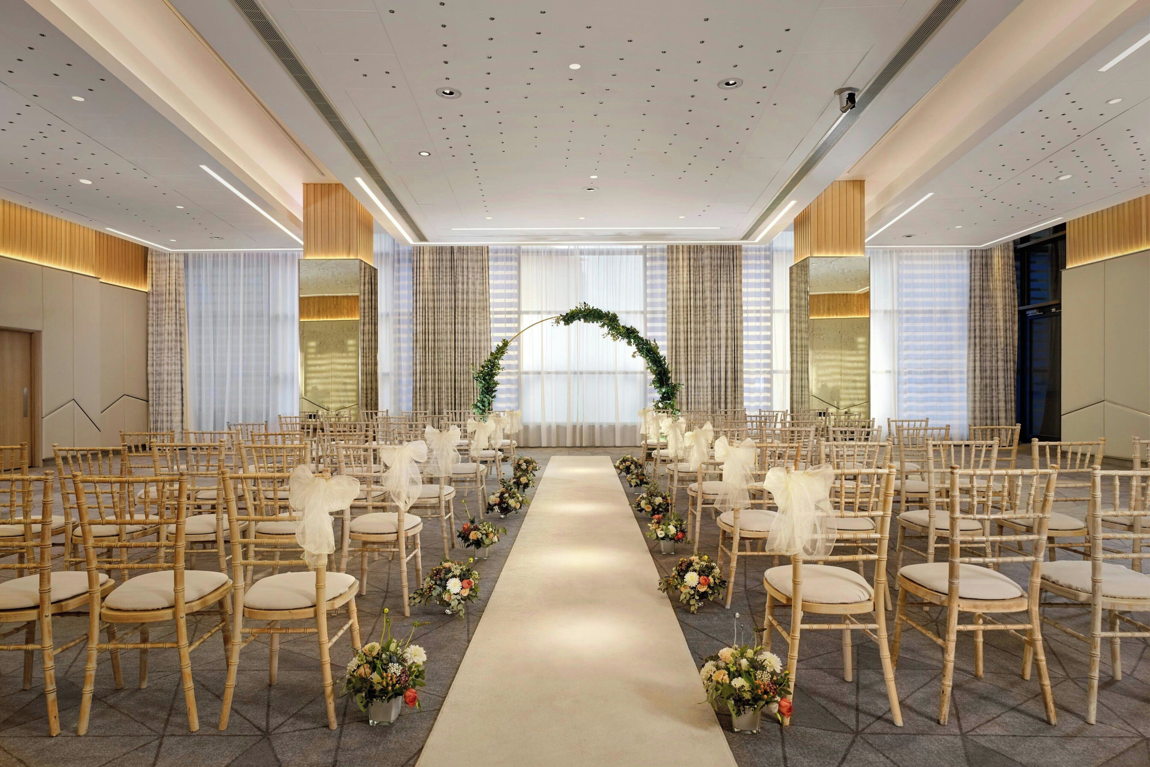 Un salón de bodas con hileras de sillas, un pasillo central y decoración floral.
