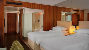 A hotel room with two beds, a mirror, a bedside table with a lamp, and a shower area.