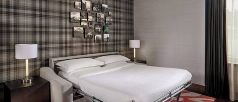 A hotel room with a bed, bedside tables, a wall-mounted picture gallery, and a window with curtains.