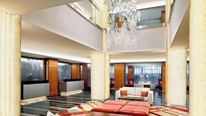 A spacious lobby with a high ceiling, a chandelier, and a seating area with sofas and a coffee table.