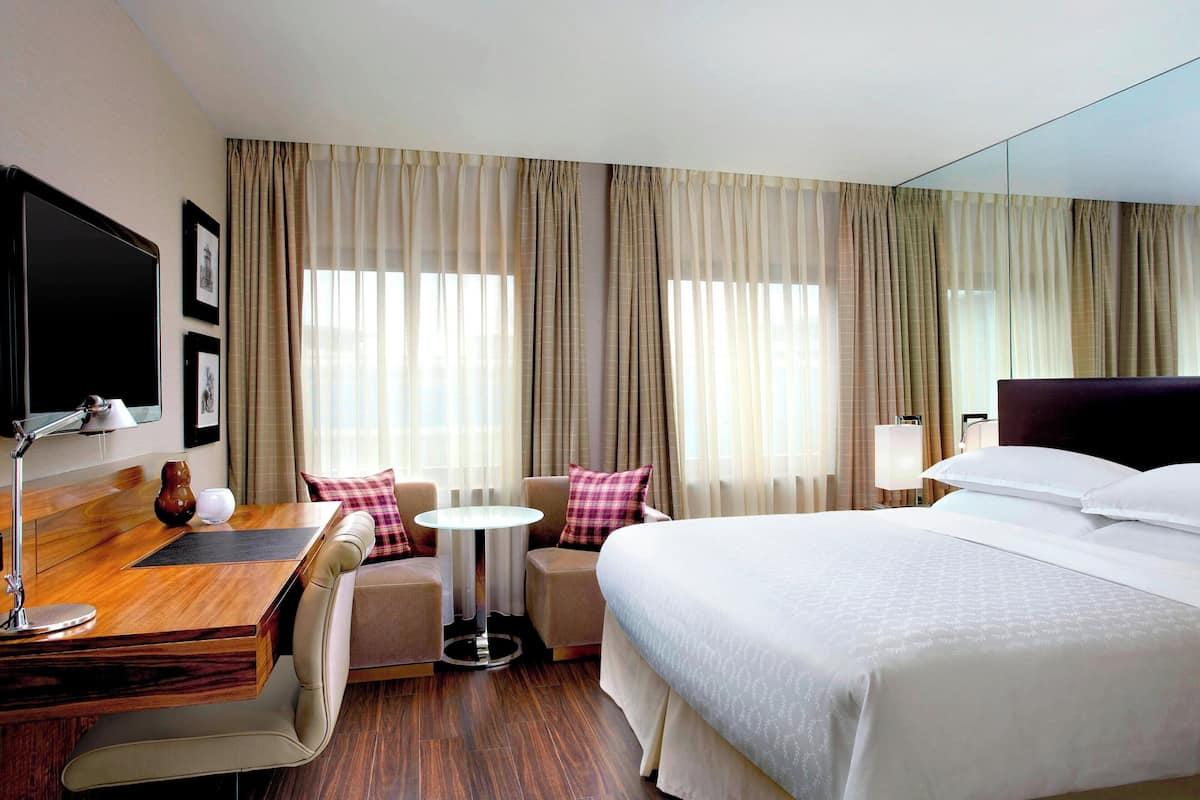 A hotel room with a bed, a desk with a chair, a small round table, and a sofa.