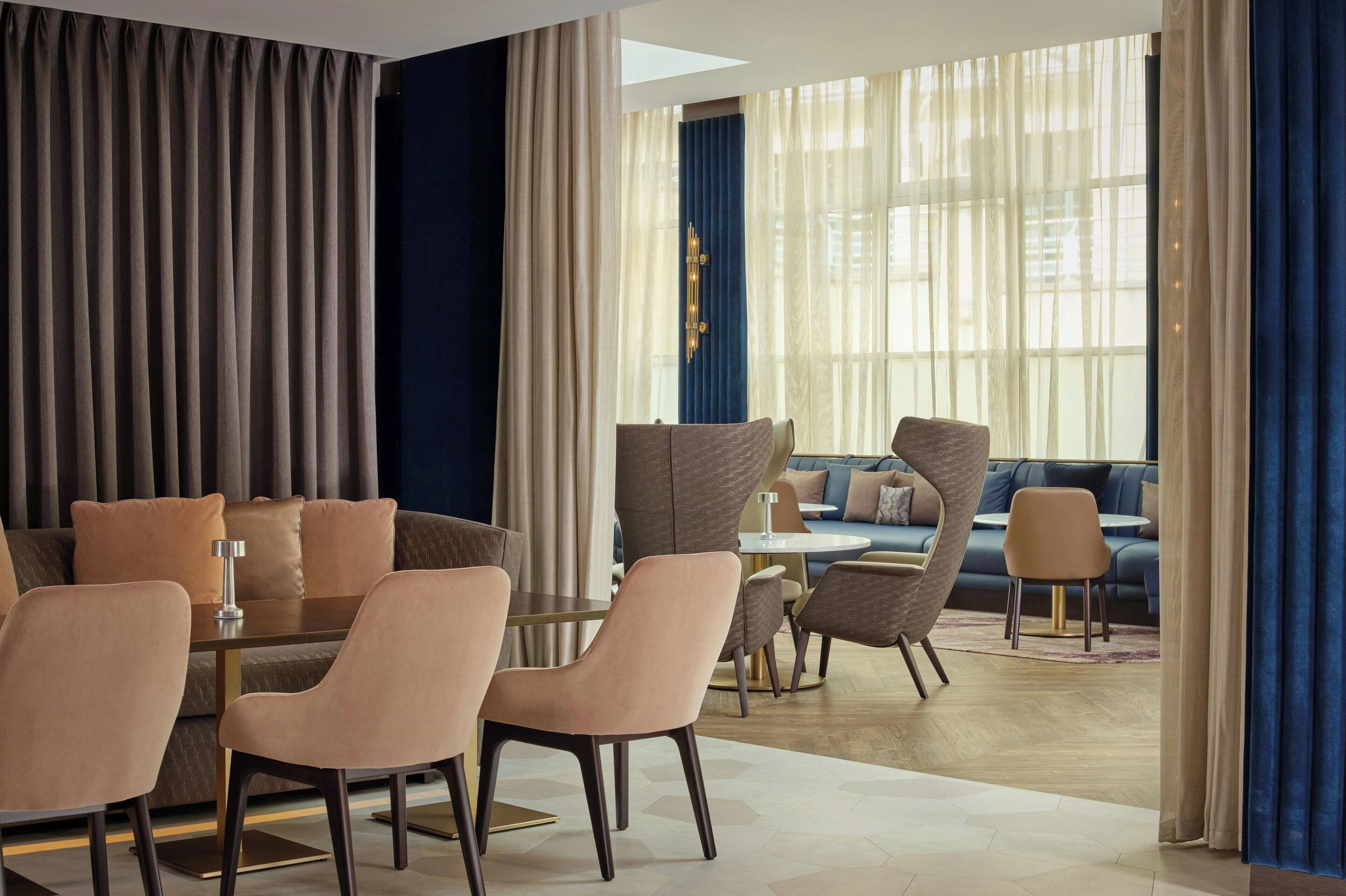 A modern hotel room with a dining area, a sofa, and a view of the city.