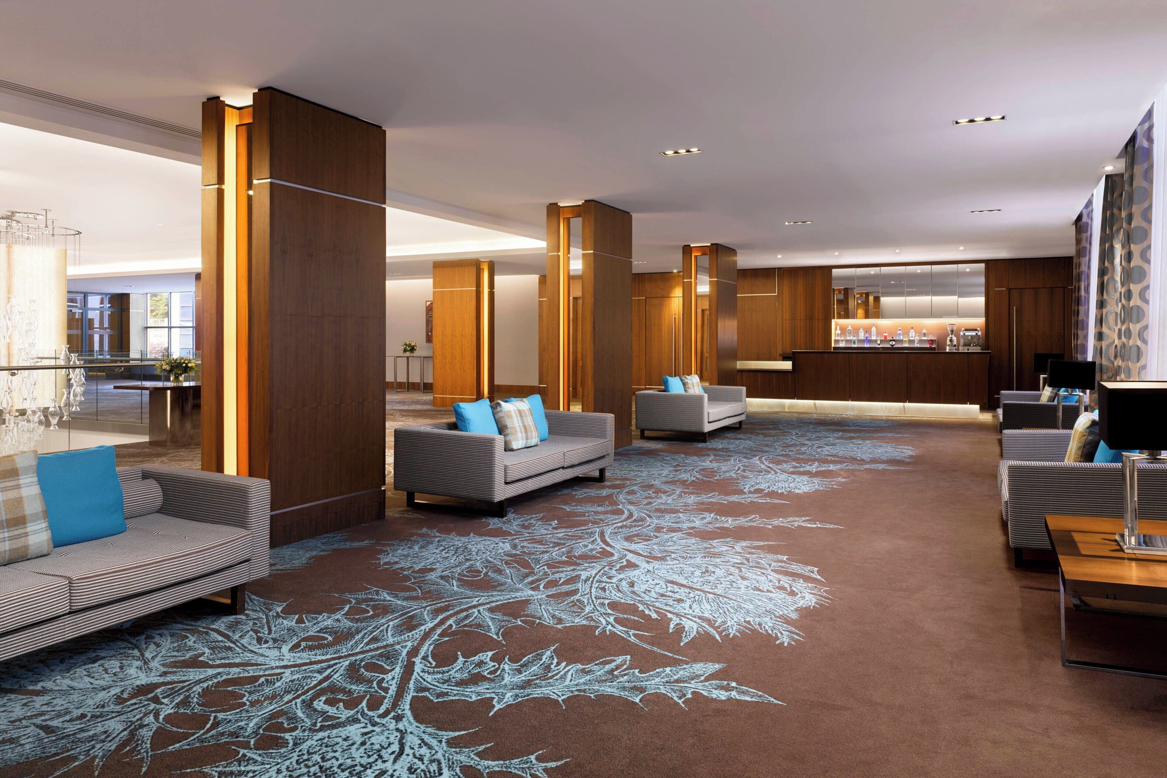 A modern hotel lobby with sofas, a bar area, and a patterned carpet.