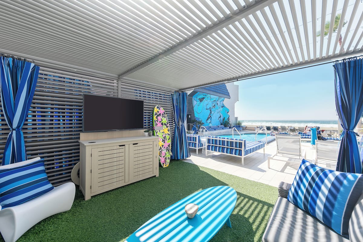 Un espacio exterior techado con piscina, asientos y una pantalla grande.