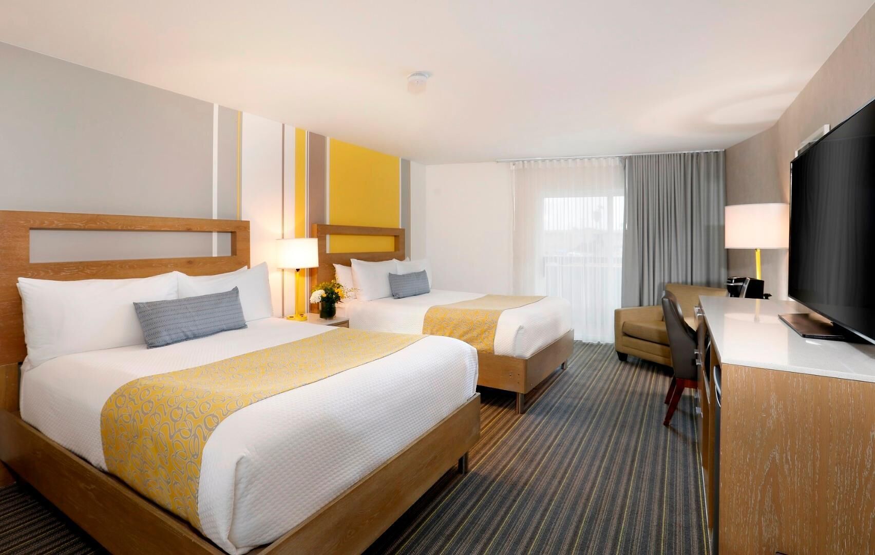 A hotel room with two beds, a desk, a television, and a window with curtains.