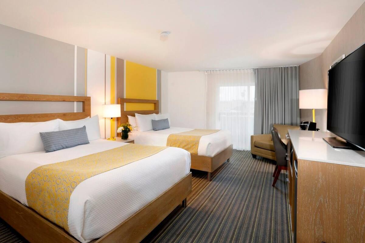 A hotel room with two beds, a desk, a television, and a window with curtains.