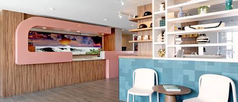 A modern interior with a wooden reception desk, a colorful mural, white chairs, and a blue tiled wall.