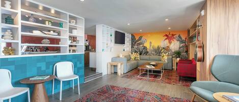 Un salon moderne avec un coin cuisine, un tapis à motifs et un téléviseur fixé au mur.