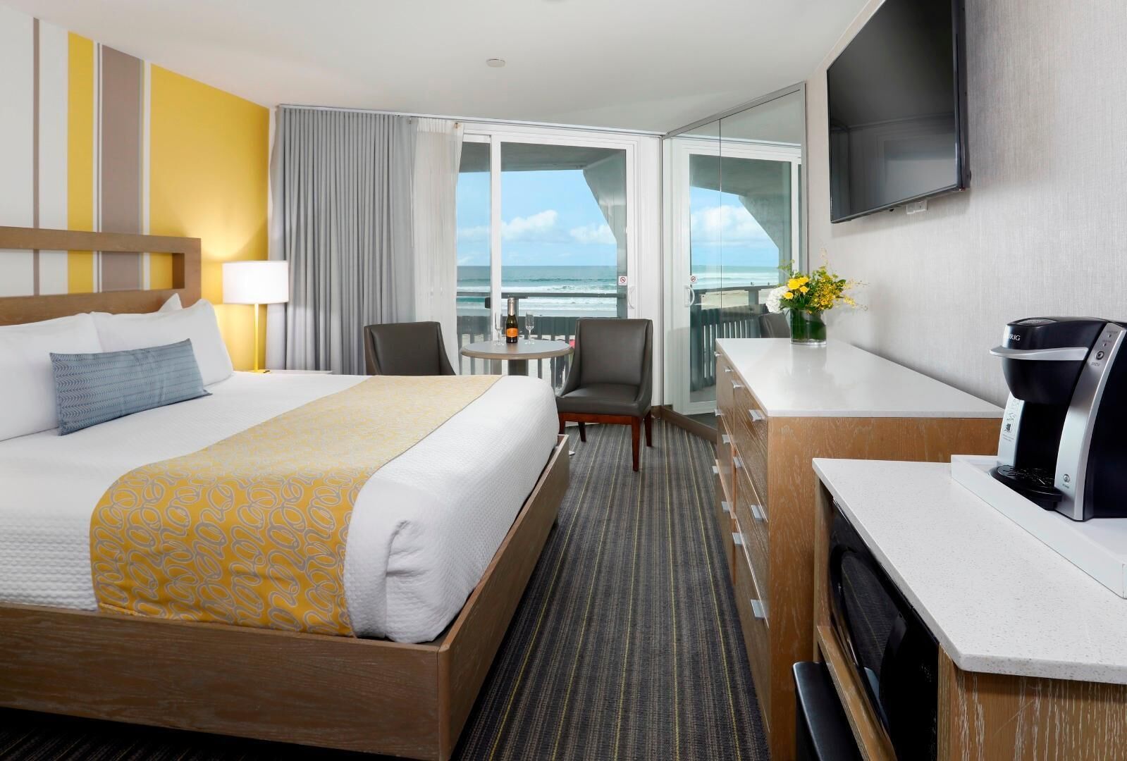A hotel room with a bed, a desk, a chair, a coffee maker, and a view of the ocean.