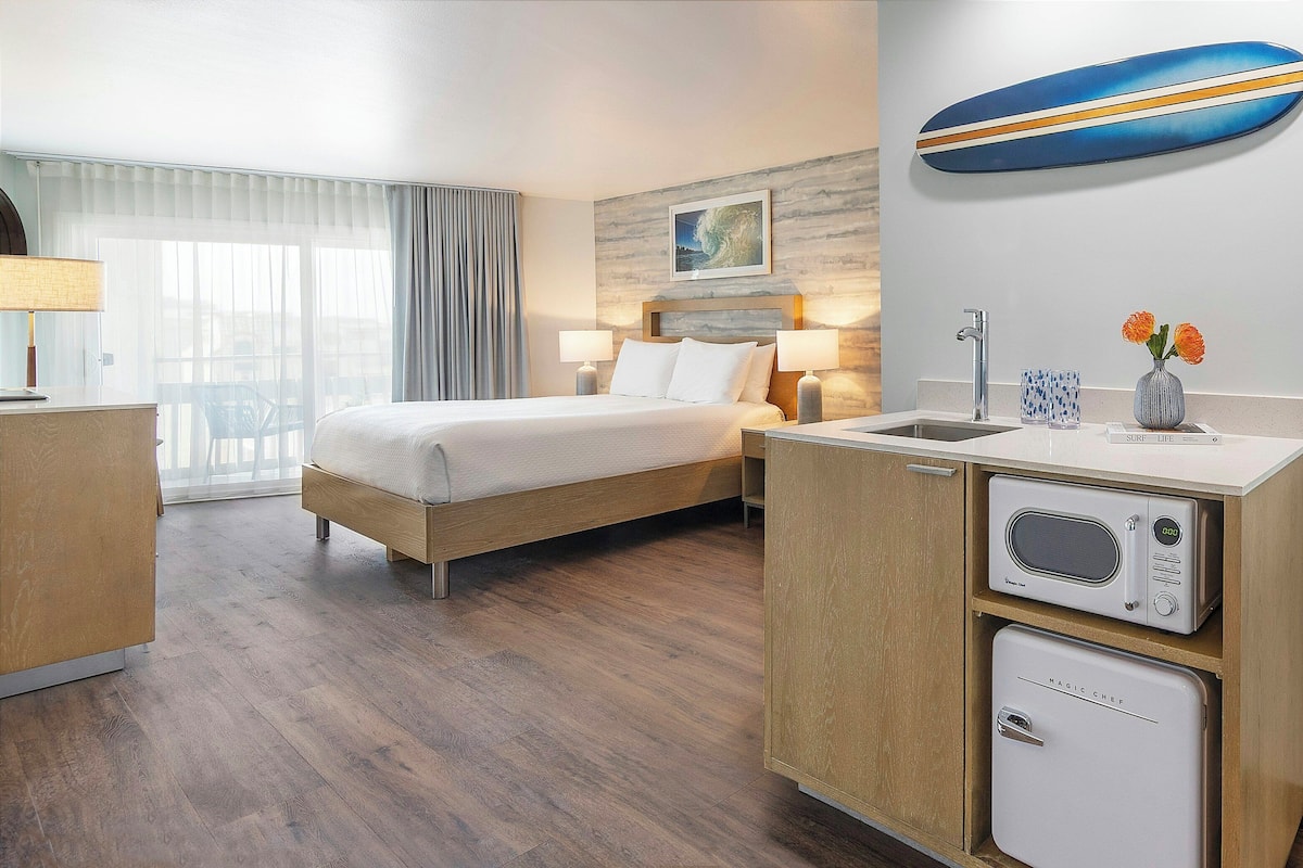 Une chambre d’hôtel équipée d’un lit, de lampes de chevet, d’un four à micro-ondes, d’un réfrigérateur, d’un lavabo et d’une fenêtre avec des rideaux.