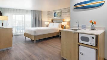A hotel room with a bed, bedside lamps, a microwave, a refrigerator, a sink, and a window with curtains.