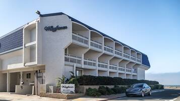 A hotel with a name sign, multiple balconies, and a car parked in front.