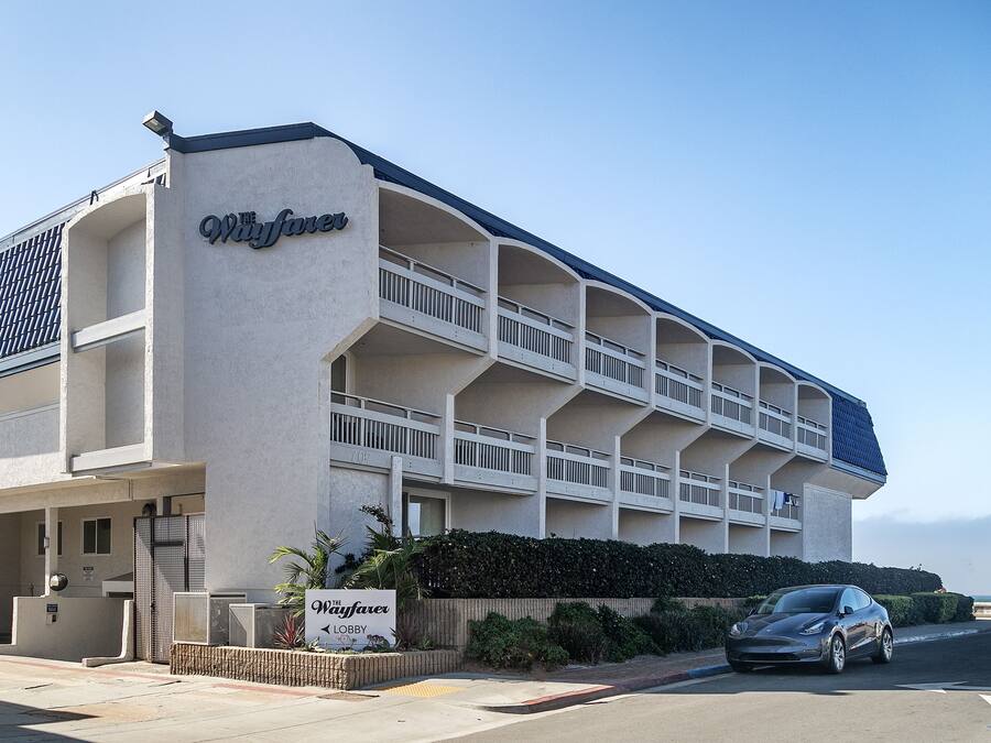 A hotel with a name sign, multiple balconies, and a car parked in front.