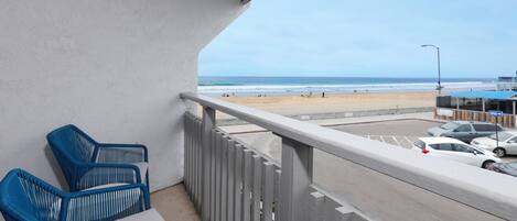 A balcony with two blue chairs, a view of the beach, and parked cars.