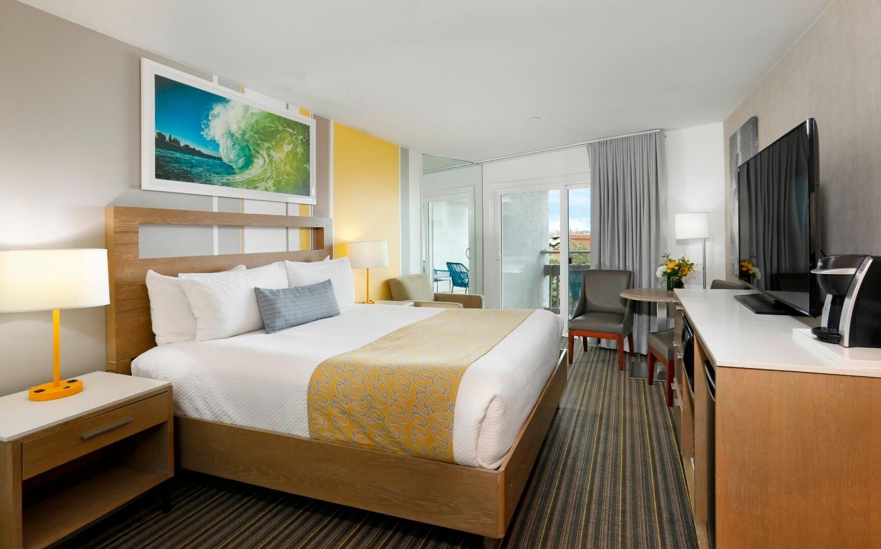 A hotel room with a bed, bedside table, lamp, chair, desk, and a TV.