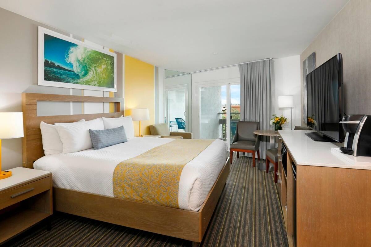 A hotel room with a bed, bedside table, lamp, chair, desk, and a TV.