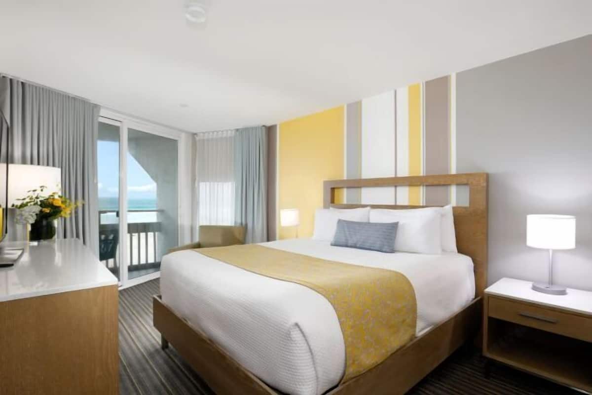 Une chambre d’hôtel avec un lit, une table de chevet, une lampe et une vue sur la mer depuis un balcon.