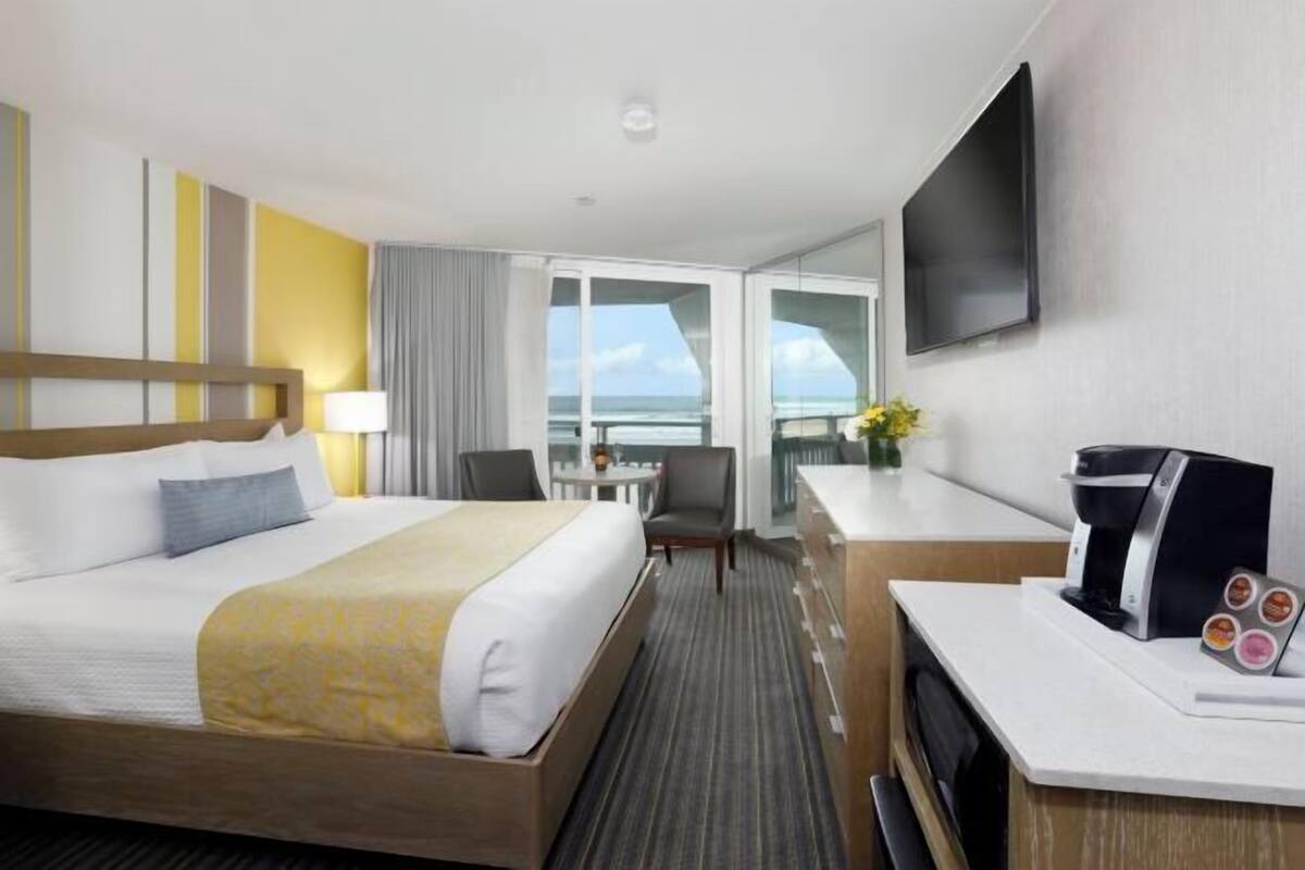 Une chambre d’hôtel avec un lit, un bureau, une chaise, une télévision et une vue sur la mer.