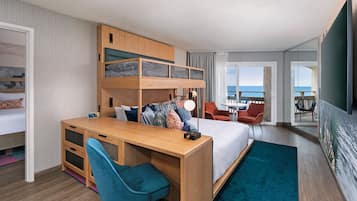 Habitación de hotel con literas, un escritorio con silla, una mesita y vista al mar a través de amplias ventanas.