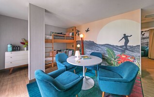 A room with a bunk bed, a round table with chairs, a lamp, and a mural of a person surfing.