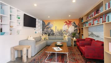 A living room with a sectional sofa, a red armchair, a coffee table, a bookshelf, and a wall-mounted TV.