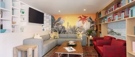 A living room with a sectional sofa, a red armchair, a coffee table, a bookshelf, and a wall-mounted TV.