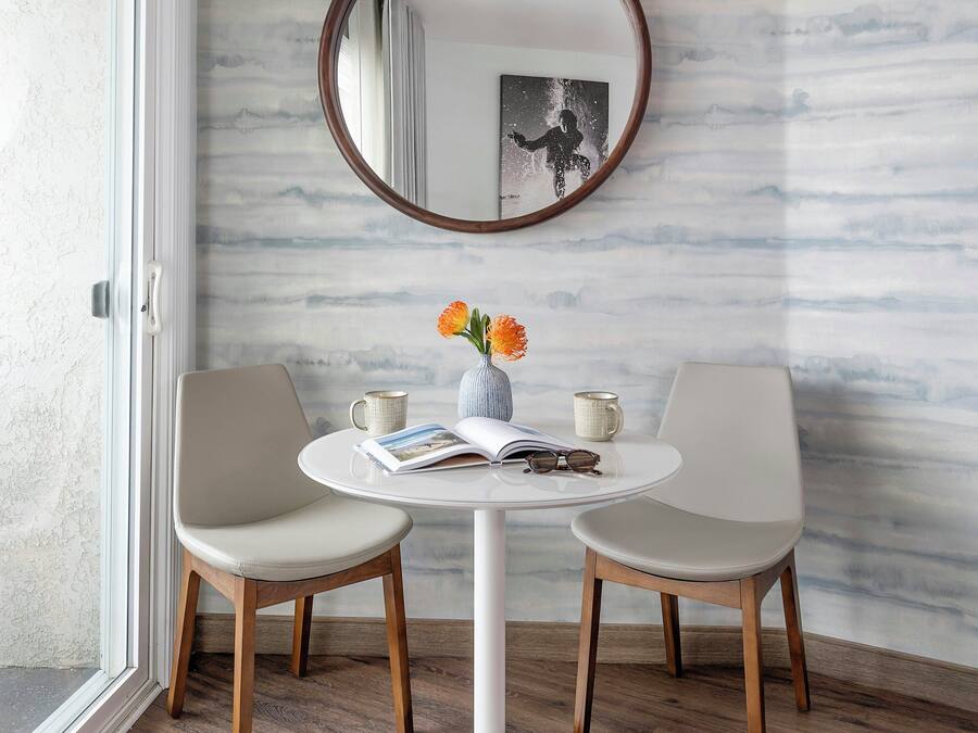 Een ronde witte tafel met twee stoelen, een vaas met bloemen en een lijst met een afbeelding aan de muur.