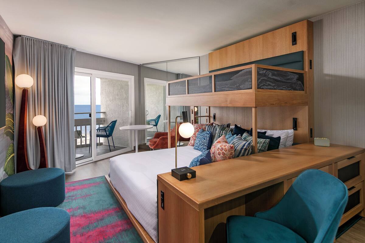 Une chambre d’hôtel moderne équipée d’un lit superposé, d’un bureau et d’un balcon avec vue sur la mer.