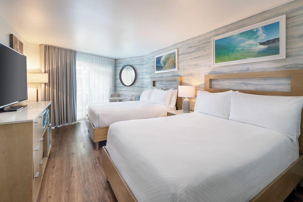 Une chambre d’hôtel avec deux lits, une télévision, un bureau et une fenêtre avec des rideaux.